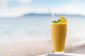Fresh mango smoothie in glass on wood with outdoor background