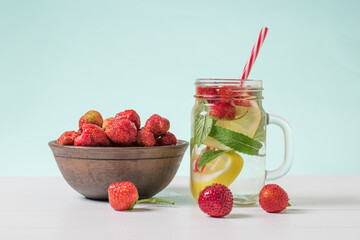 A bowl of strawberries and a mug of cold water and berries on a white table.