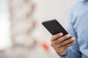 Close up male hands holding using black smartphone on city background.