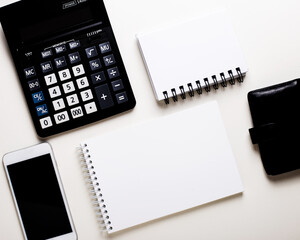 White notepads, black wallet, phone and calculator lie on a white table. Flat lay. Business concept