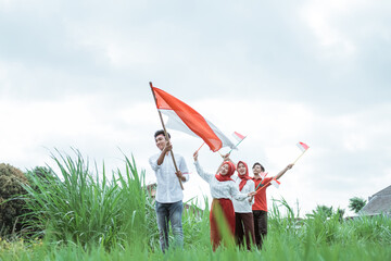 boy in white walking carrying an Indonesian flag with stick and three of his friends walk behind him with a small flags