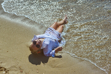 A little girl is resting at a seaside resort . A happy child in a white shirt takes a sun bath on the sea