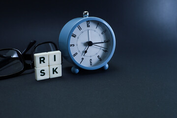Block letters on risk, alarm clock, and eyeglasses on black table 