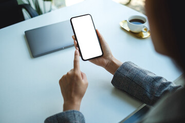 Top view mockup image of a woman holding and pointing finger at a mobile phone with blank white desktop screen