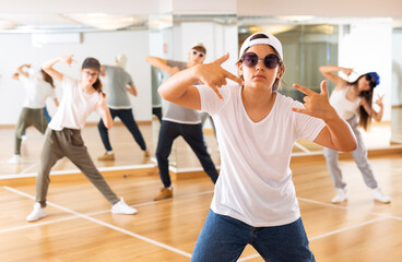 Fototapeta na wymiar Portrait of emotional teenager girl doing hip hop movements during group class in dance studio
