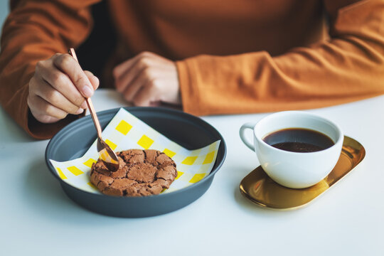 Closeup image of a woman eating delicious chocolate cookie with hot coffee