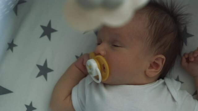 Handsome little boy sleeping sweetly in his crib. Infant sucks a pacifier and falls asleep under a baby mobile 4k