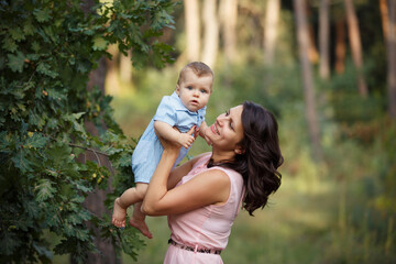 Happy family in a summer park. Family day. Little Boy with parents weared in casual green. Sunny summer day outdoors. Mother is holding her little son in hands. Waik in nature forest