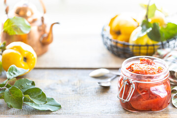 Homemade quince jam in a glass jar on an old wooden background. Fresh fruits and leaves of eggs around a jar. Horizontal photo. Copy space.