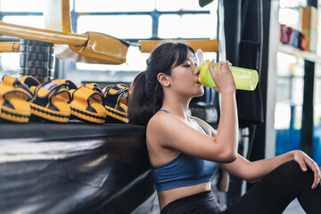 Sporty young asian woman holding bottle of protein shake and drinking