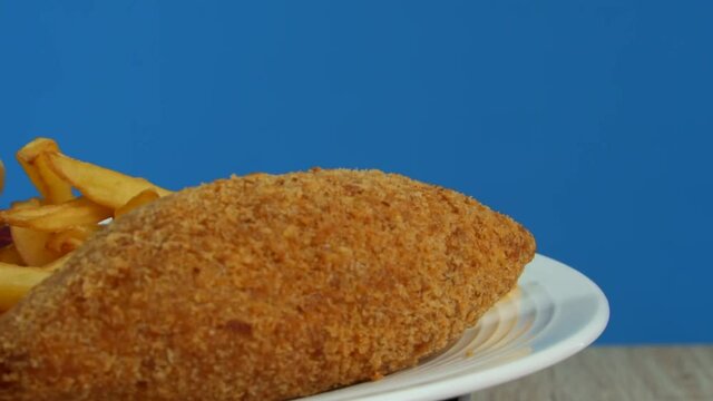 French fries with Kiev cutlet with red sauce spinning on a blue background