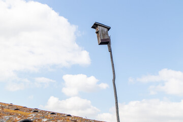 Birdhouse on a wooden stick on the roof against the blue sky with clouds