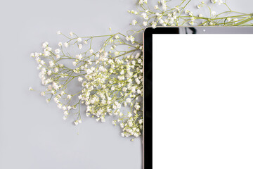 part of the tablet with a place to insert in the corner of the frame next to the hypsophila flowers on a gray background.