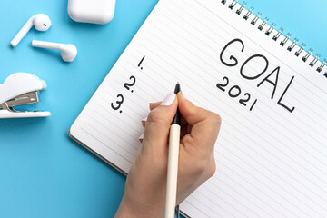 Girl writes in notepad of goal for 2021 on a blue background