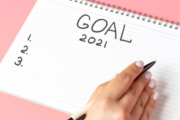 Girl writes in notepad of goal for 2021 on a pink background