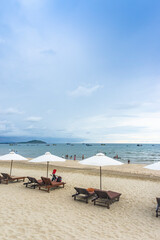 Fototapeta na wymiar White sand beach with chaise chairs and white umbrella in clear blue sky with many tourists at Muine Bay Resort, Mui Ne, Phan Thiet city, Binh Thuan province, Vietnam