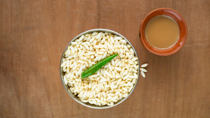 puffed rice and a green chili on a steel bowl with fresh hot tea on a wooden table top 