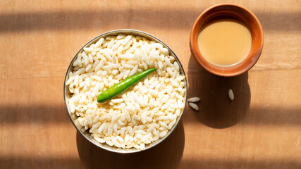 puffed rice and a green chili on a steel bowl with fresh hot tea on a wooden table top 