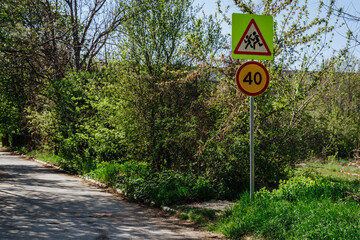 Two road signs on one pillar caution children sign and speed limit sign 40. Signs on the background of branches and blue sky on the street on a sunny day.