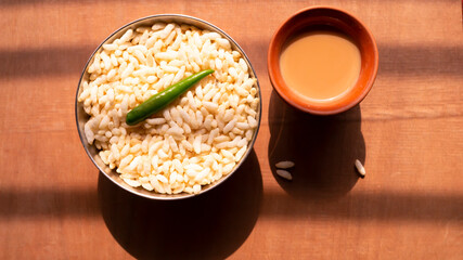 puffed rice and a green chili on a steel bowl with fresh hot tea on a wooden table top 