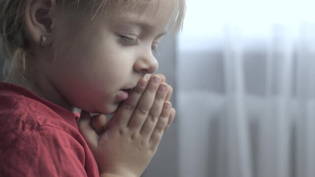 little daughter lifestyle girl makes a wish prayers bedtime religion concept . prayer child indoors praying by bed in front of window