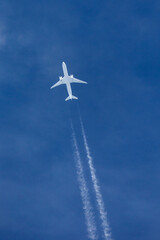 Large twin engined commercial airliner jet aircraft flying at high altitude with a large contrail flowing behind it.