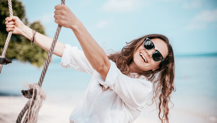 Young beautiful curly woman girl swinging and having fun on a swing on a tropical beach vacation...