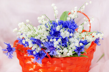 Lilies of the valley and cornflowers in orange basket