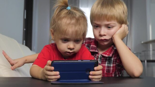 children watch online video on a smartphone. little boy and girl brother sister watch online streaming lifestyle broadcasting cartoons on the phone