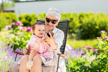 family, generation and people concept - happy grandmother and baby granddaughter with smartphone at...