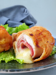 Chicken cordon bleu schnitzel, meat wrapped around ham and cheese, breaded and fried on plate, vertical