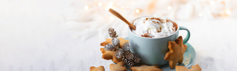 Hot winter drink: chocolate with whipped cream in blue mug. Christmas time. Cozy home atmosphere, white background. Homemade gingerbread cookies, christmas lights. Banner, copy space for text