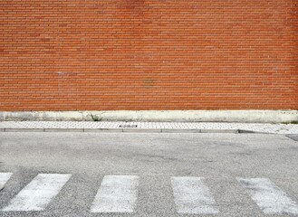 Brick wall with a  sidewalk made of concrete tiles and a weathered  asphalt street with crosswalk. Background for copy space