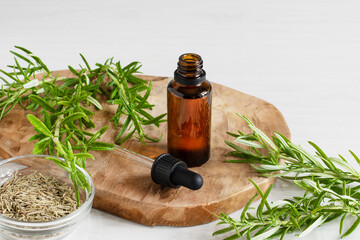 Rosemary essential oil and fresh rosemary branch on wooden background.