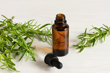 Rosemary essential oil and fresh rosemary branch on wooden background.