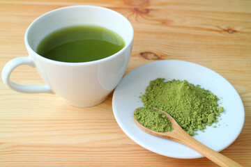 Cup of Hot Matcha Green Tea with a Plate of Matcha Tea Powder on Wooden Table