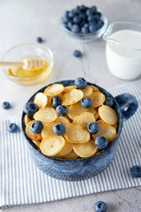 Blue Bowl of mini pancake cereal with blueberries, maple syrup and milk on concrete background. Tiny pancakes, new food trend concept. Cute healthy breakfast or snack. Recipe, menu.