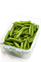 Garden peas in pods freshly picked in a plastic container,  isolated on a white background.  Grow your own concept