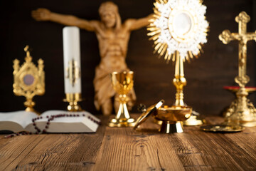 Catholic religion symbols. The Cross, monstrance, Jesus figure, Holy Bible and golden chalice on the rustic wooden altar.