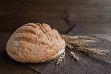 Fresh soft bread with a crispy crust on a brown wooden background with wheat ears.