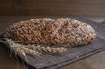 Dry bread with a crispy crust sprinkled with sesame seeds on a brown linen napkin and a wooden...