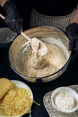 Woman in checkered apron and black gloves mixing yeast dough with wooden spoon. Process of making bakery. Adjarian Khachapuri Recipe – Georgian cheese bread.
