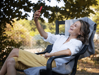 Fototapeta na wymiar Young beautiful girl woman talking on a smartphone in the summer in the garden of his house sitting on a chair