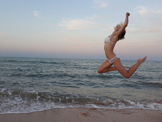 Happy teenage girl playing and jumping on the beach at the seaside in sunset