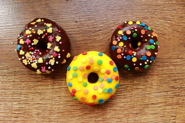Assorted donuts on a wood background. Rainbow dots decoration. Brown sugar. Lemon, melon, pineapple, mango, banana flavour. Chocolate