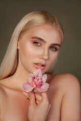 Obraz na płótnie Canvas Beauty face. Natural skincare. Blonde woman with bare shoulders holding orchid flower isolated on brown.