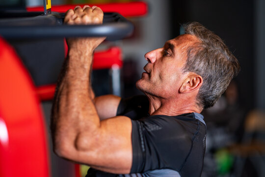  man strengthening his muscles by doing pull-up on horizontal bar in a fitness center