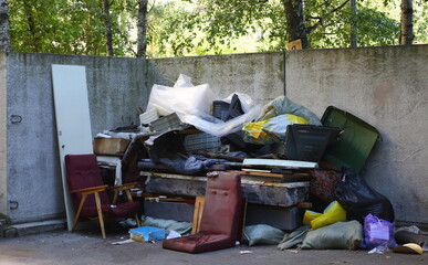 A pile of household garbage at the gray concrete wall of the dump