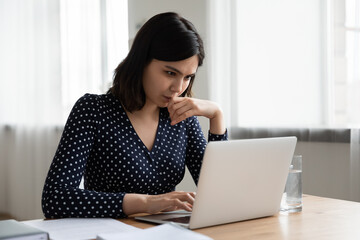 Thoughtful Vietnamese millennial girl sit at desk at home study online on laptop pondering of problem solution, pensive Asian young woman work with document on computer thinking contemplating