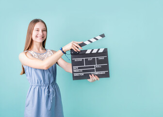 Happy smiling teenager girl in a blue dress holding a clapper board isolated on blue